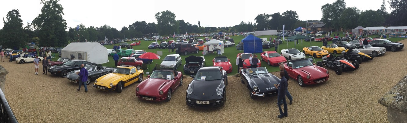 PHEA ROADSHOW: Kimbolton Charity Car Show - Sunday 10th July - Page 2 - East Anglia - PistonHeads - The image captures an open grassy field which has been transformed into a makeshift parking lot. It is filled with a diverse array of cars and motorcycles. The vehicles are parked in a manner that creates an organized yet visually striking pattern on the grass. Some cars are densely packed while others are more spaced out. The variety of vehicles suggests a mixed crowd or event. The field is surrounded by trees, and the sky is visible in the background, providing a natural backdrop to the scene. The image is taken from a bird's-eye perspective, giving a comprehensive view of the layout and arrangement of the vehicles.