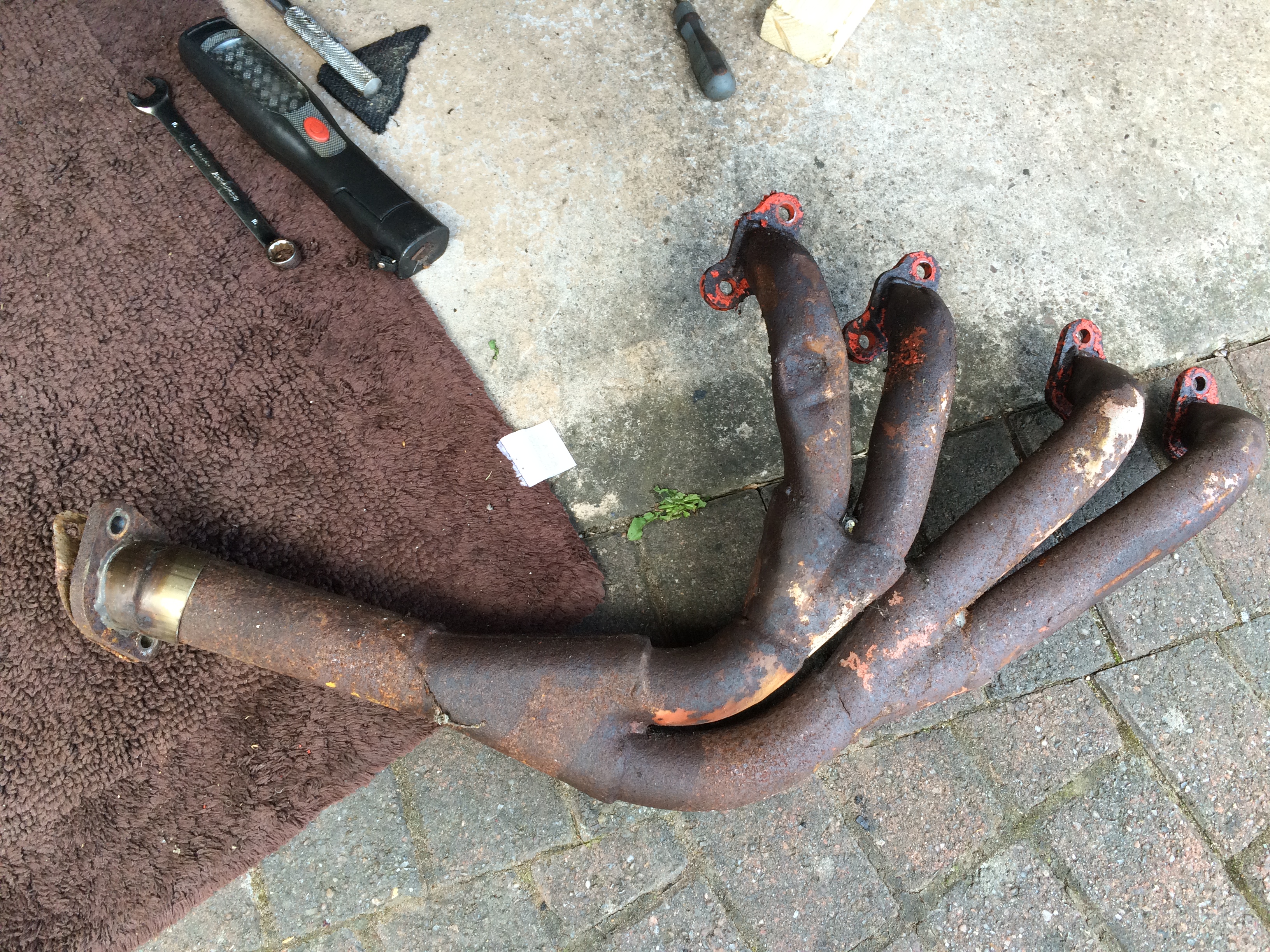 What's happening in your garage this weekend ? - Page 153 - Wedges - PistonHeads - The image shows an outdoor scene on a brick pavement, with a focus on a dirty, rusty pipe lying on its end. The pipe appears to have been disconnected, as evidenced by the presence of fittings that match the pipe's ends. A wrench is visible, possibly indicating that someone might have been working on the pipe. The ground is dirty, with signs of wear and potential repairs.