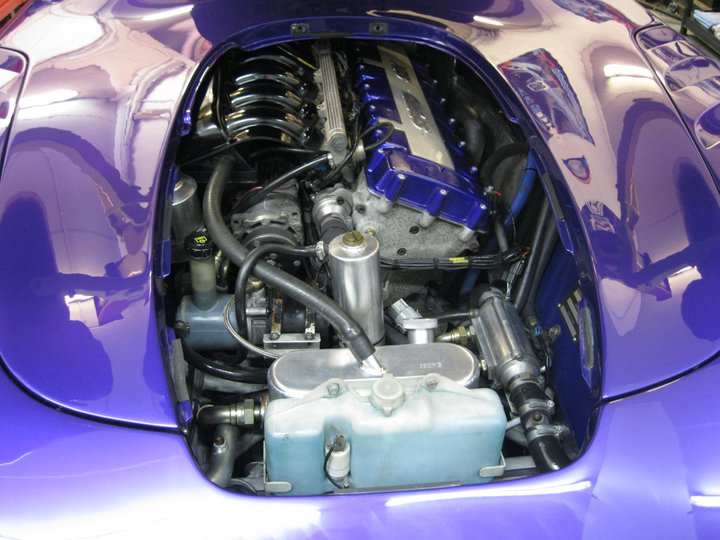 Show us your powder coloured engines - Page 6 - Speed Six Engine - PistonHeads - The image is a close-up photograph of the engine compartment of a blue-colored car. The car's cooling system is visible, with a blue coolant reservoir and a series of metal radiator fins. The engine components, such as the intake manifold, exhaust headers, and accessory belt drive systems, are prominently displayed. The car is also equipped with blue engine stops, which have a curved shape, and the hood has a shiny, reflective surface. The shiny surface suggests that the car is well-maintained, reflecting its cleanliness in this view.
