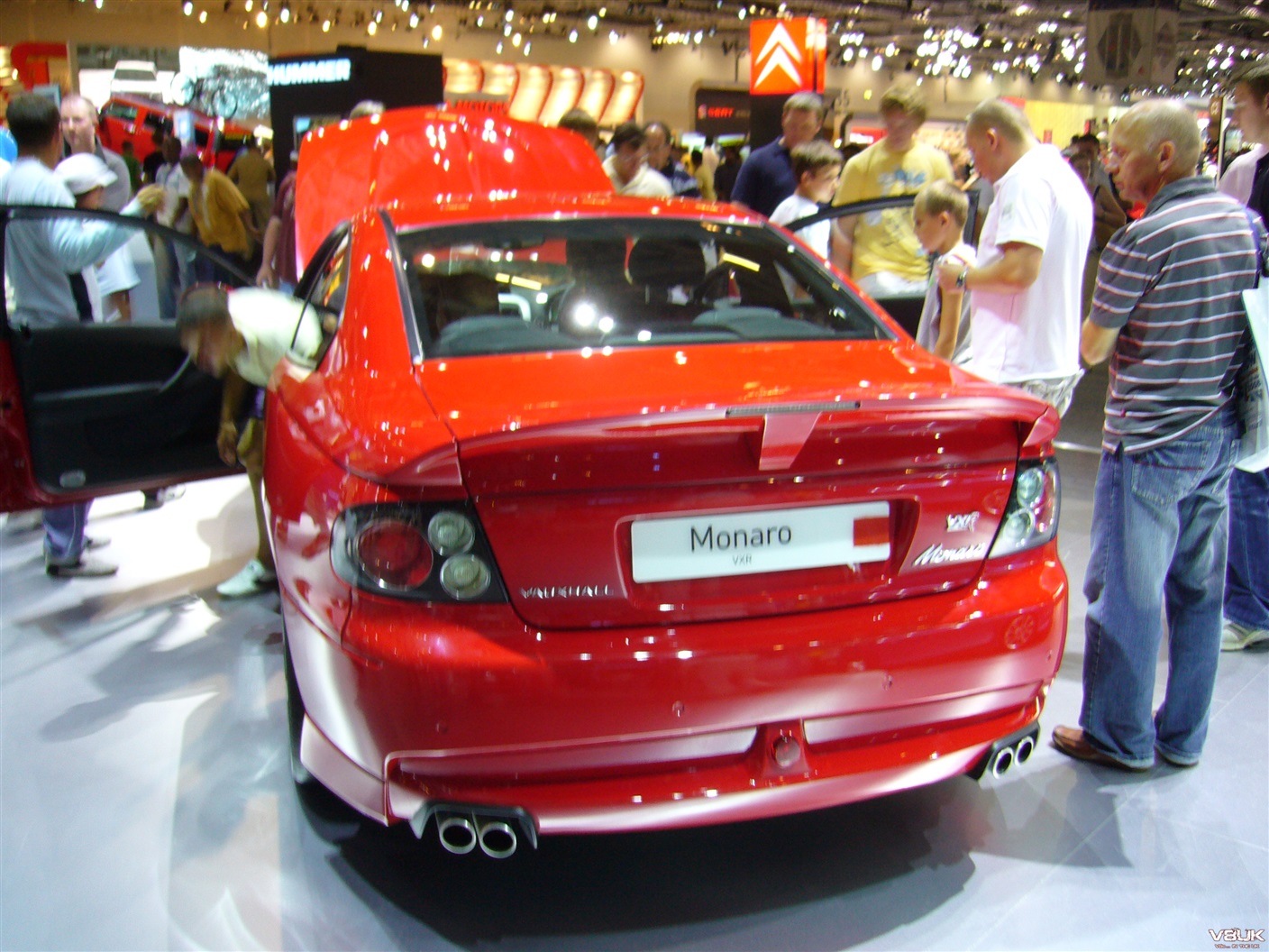 Why did you buy yours? - Page 3 - HSV & Monaro - PistonHeads - The image shows a red sports car on display at what appears to be a car show or exhibition. The car is sleek and shiny, with a design that suggests speed and performance. It's parked indoors, possibly under a tent, given the lighting conditions. In the background, there are several people observing the vehicle. They seem interested in the car, as they are looking at it closely. There is also some signage or banners visible, which might be related to the exhibition or the brand of the car. The atmosphere suggests a well-attended event where enthusiasts gather to admire and discuss various models of vehicles.