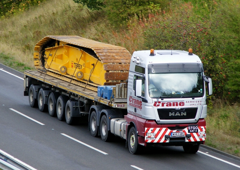 Spotted Forthright MC - Page 34 - Herts, Beds, Bucks & Cambs - PistonHeads - The image depicts a semi-truck transporting two large pieces of machinery on a multi-lane highway during the day. The truck has a long trailer carrying the equipment, and it bears the writing "CRANE MOVERS - LONDON" on the side. The highway the truck is on appears to have lane markers and is bordered by grassy embankments.