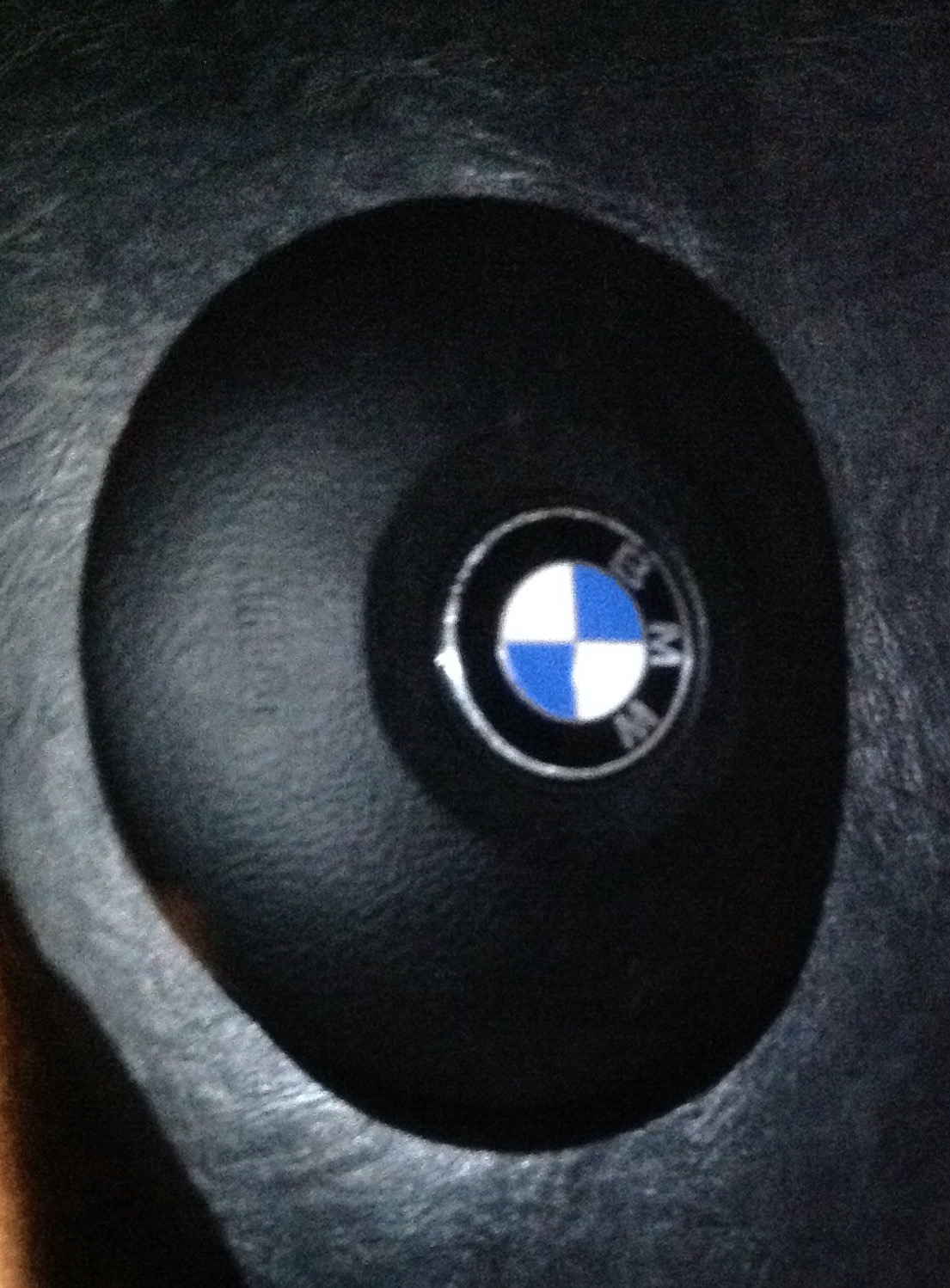 BMW E46 330dA Touring - Page 14 - Readers' Cars - PistonHeads - The image shows a circular object with a prominent logo in its center. The logo consists of two interconnected arrows forming a circle, with a white, blue, and red checkerboard pattern at the top of the arrows. The background of the image is black and appears to be a textured surface. The lighting is focused on the object, creating a soft shadow behind it. The object itself seems to have some texture, adding depth to the image. The shoe is well cared for, suggesting it might be a valuable piece of equipment.