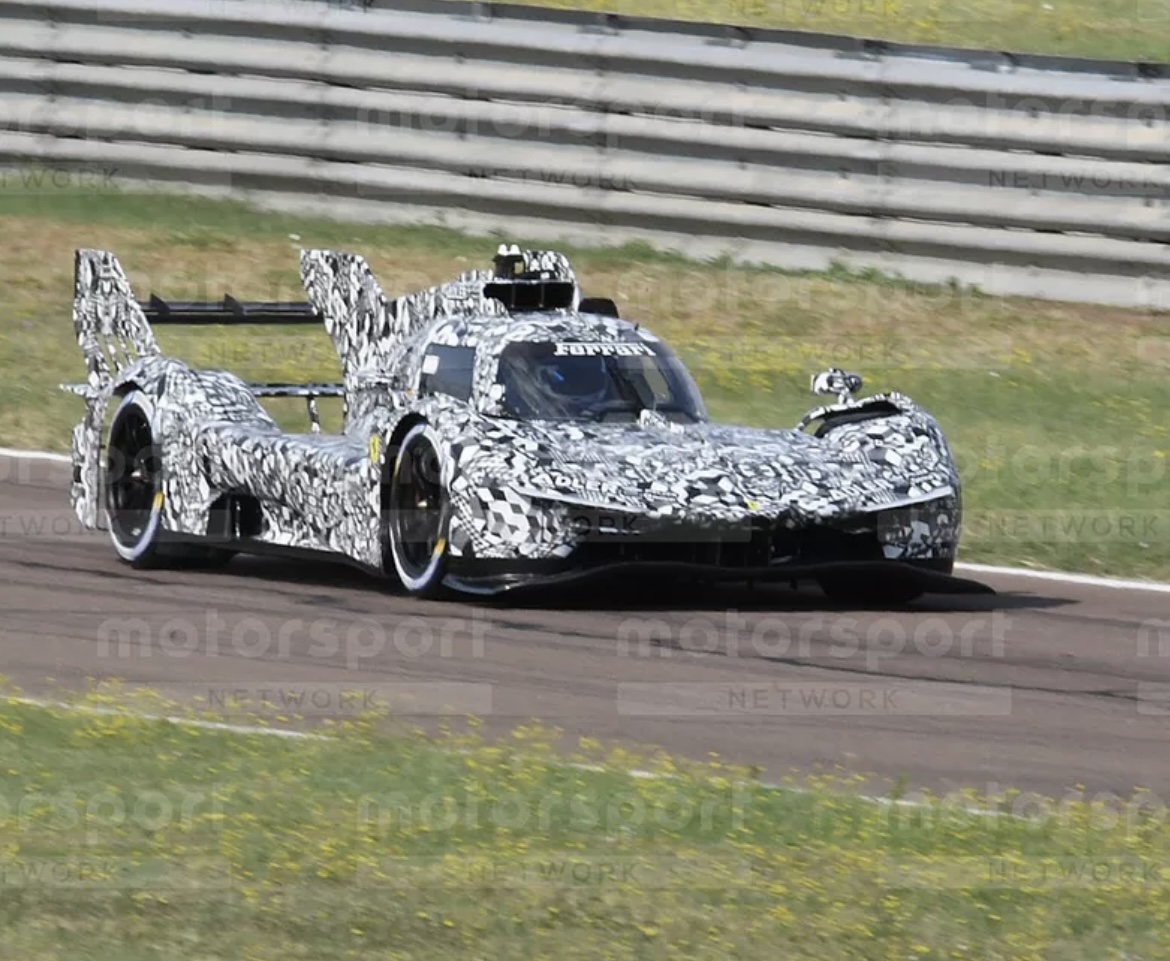 New cars  - Page 1 - Le Mans - PistonHeads UK - The image shows a sports car in motion on a race track. The car is predominantly white with a camouflage pattern over the body, suggesting it might be a prototype or undergoing testing. It features a large front spoiler and rear wing for aerodynamic downforce. The vehicle has black tires and seems to have a number of sensors and equipment on top of it, which is typical for a racing car. In the background, there are multiple race tracks visible, indicating that this image might have been taken at a motorsport event or venue.