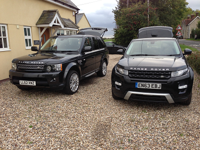 A truck parked on the side of a road - Pistonheads - The image features two Range Rover sports cars parked on a gravel driveway in front of a yellow house, possibly a suburban or rural setting. Both cars are black and have their sunroofs open. There appears to be a trailer attached to one of the vehicles. The sky is overcast, suggesting it might be a cool or cloudy day. The vehicles are positioned facing the viewer, providing a view of their front and side profile.