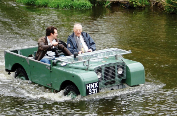 What's the best summer car? - Page 3 - General Gassing - PistonHeads - In the image, an older man and woman are enjoying a ride in a green jeep on what appears to be a river or creek. The water level is halfway up the sides of the vehicle, suggesting gentle movement across the water body. They are both seated comfortably inside the jeep, which has a removable top, indicating that they might be experiencing an open-air ride. Both individuals appear relaxed and engaged in their outing. In the background, there's another person partially visible near a bench, possibly observing the jeep ride or simply enjoying the surrounding environment. The overall atmosphere is one of leisure and exploration.