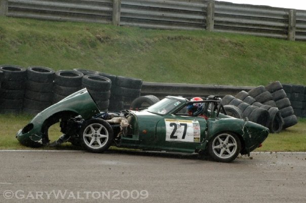 G27 mystery. - Page 1 - Ginetta - PistonHeads - The image shows a vintage racing car that appears to have been crashed into a barrier, with the back end of the car visibly damaged. The car is green and has the number 27 prominently displayed. Behind the crash are multiple sets of tires laid out, possibly indicating a track or testing area. The surrounding grassy field indicates an outdoor, possibly amateur racing environment.