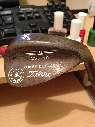 Help Golf clubs - Page 1 - Sports - PistonHeads - The image shows a brown putter golf club with two white capped polish bottles in the background. The club features a vintage design and has the words "VOKERY DESIGN" printed in white on it. There is also text that reads "265-10" and "TITLEIST," indicating the brand of the club. The club is placed on a wooden surface, possibly a desk, which is the main focus of the photograph. The lighting suggests an indoor setting. The photo captures the club in a close-up, emphasizing its design and the words printed on it.