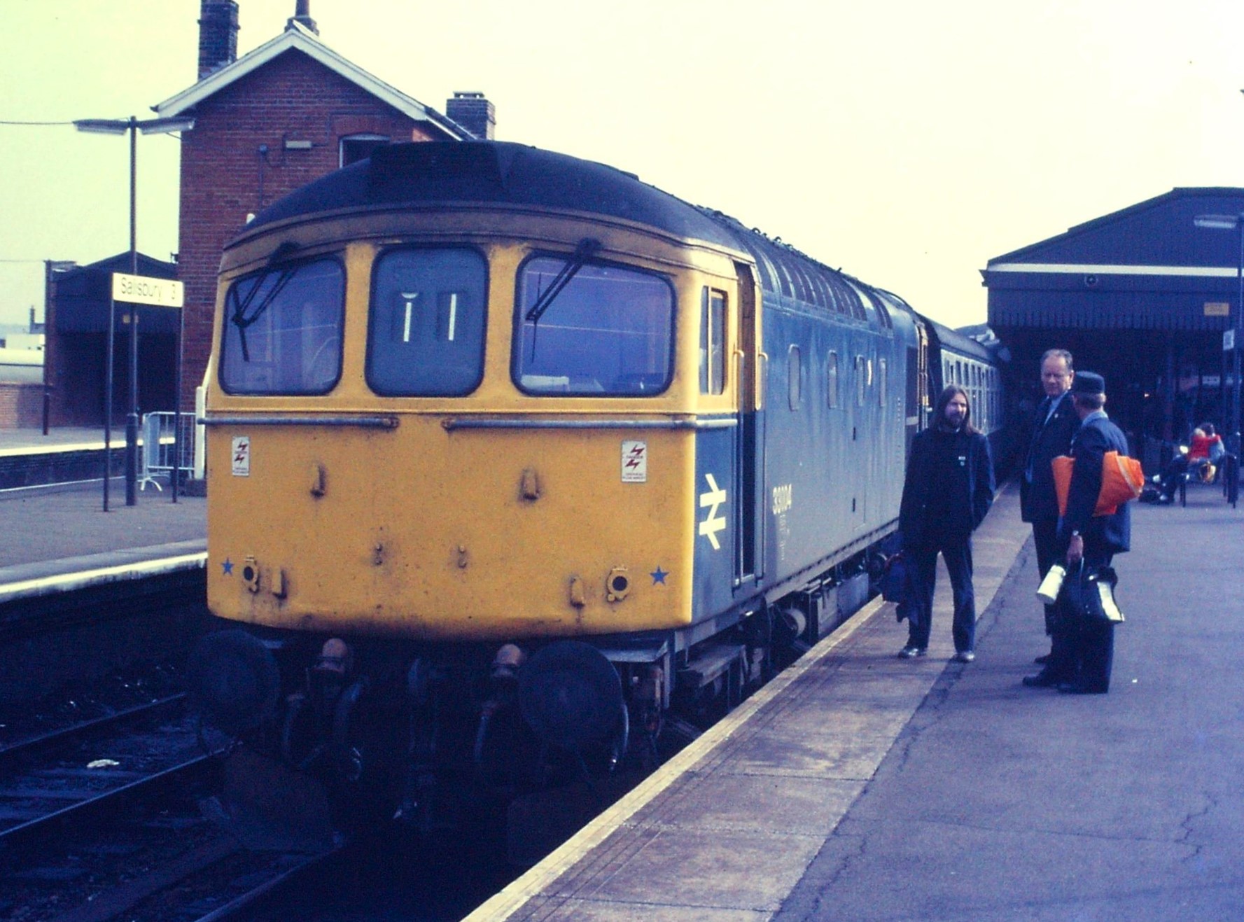 Loco sheds and other railway buildings... - Page 35 - Boats, Planes & Trains - PistonHeads UK - The image shows a train station scene. A large yellow diesel locomotive is parked at the platform with its front facing the camera. The locomotive has the number 20 on the side, indicating it may be part of a railroad company's fleet. On the platform, there are two people standing at a distance from the train. They seem to be waiting or perhaps just arrived. Behind them, another train can be seen parked further away, suggesting this is a busy station. The overall scene suggests a day in the life of commuting by rail.