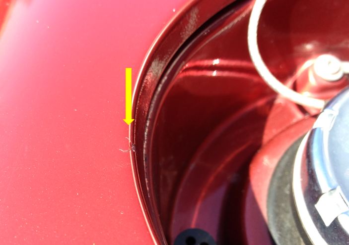 Chip away or respray...? - Page 1 - Aston Martin - PistonHeads - This image shows a close-up view of a car's tailgate area. The main focus is a marked spot on the red tailgate, with a yellow arrow pointing to this area, indicating an object to inspect or a possible repair location. This appears to be part of an inspection or maintenance process. The tailgate, made of a glossy material, reflects light and adds to the image's detail. The style of the arrow suggests that the viewer is asked to pay attention to this exact point.