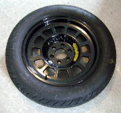 viper oem spare wheel  - Page 1 - Vipers - PistonHeads - The image shows a single circular tire lying flat on its rim. The tire appears to be a spare or perhaps for a lighter vehicle, given its size relative to the background. The rim around the tire has multiple bolt-like features, likely for attaching it to a vehicle. The color of the tire is uniformly black, with a more textured pattern visible on the sidewall. The background is a simple, neutral color, allowing the tire to be the focal point of the image.