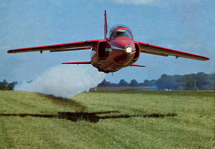 Just awesome vehicle-related images. - Page 12 - General Gassing - PistonHeads - The image captures a dynamic scene of a red fighter jet soaring through the sky. The jet, with its afterburner glowing brightly, is seen flying low over a field. The field in the foreground is lush green and slightly blurred due to the airplane's speed. The background is a clear blue sky, adding to the sense of motion in the image. The entire scene conveys a sense of power and speed synonymous with aviation and from fighter planes in particular.