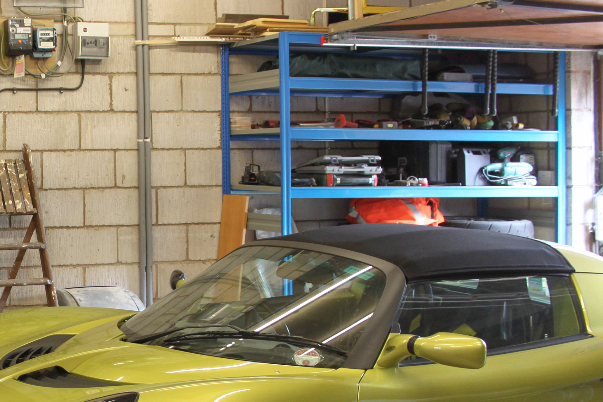 Pistonheads - The image shows a vibrant yellow sports car inside what appears to be a garage or workshop. The car is parked and the interior of the vehicle is visible, featuring black upholstery on the seats and dashboard. In the background, there's an array of other vehicles and equipment, suggesting a space dedicated to automotive maintenance or repair. There are tools and parts on shelves and workbenches, indicating that this is not only a storage space for vehicles but also an active workspace. The setting appears to be a professional environment, possibly in a shop specializing in exotic or luxury cars.