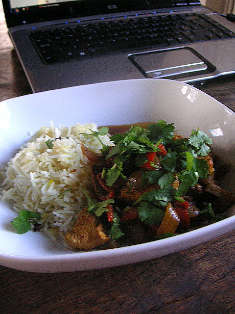 Photo of your Lunch - Page 3 - Food, Drink & Restaurants - PistonHeads - The image showcases a meal served on a wooden dining table. A white plate is the centerpiece, holding a serving of spaghetti topped with a generous portion of fresh, green basil, sliced red peppers, and beans. Adjacent to the plate, a laptop is open and placed, possibly suggesting a work from home or study setting. A soft light illuminates the scene, casting gentle shadows and adding a cozy ambiance to the setting. The meal appears to be well-prepared, offering a delightful view of a home-cooked meal being savored in comfort.