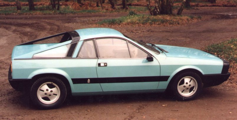 Pistonheads Lets Lancias - The image features a vintage, two-door sports car with striking turquoise and black panels. The vehicle's design includes a distinctive rear spoiler and side window rims. The sports car is parked on a patch of dirt or gravel, and the background shows lush greenery and possibly trees, suggesting a natural or park-like setting.