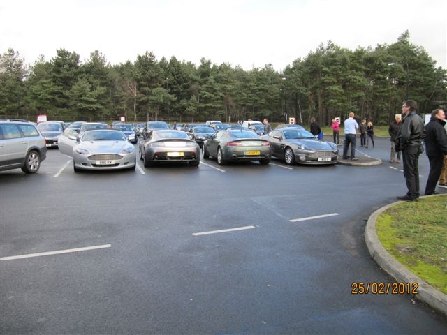 Fleet Services this morning - Page 1 - Aston Martin - PistonHeads - The image shows a large parking lot filled with various cars, suggesting this may be a popular destination or a busy time of day. People are scattered throughout the scene, standing and possibly conversing in small groups. The sky overhead appears to be overcast with no visible signs of rain or snow. The photograph is timestamped, indicating it was taken on "25/02/2012," displaying a specific date.