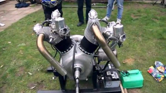 OFFICIAL GG YOUTUBE Thread, MUST HAVE DESCRIPTIVE TITLES - Page 12 - General Gassing - PistonHeads - The image shows an outdoor setting with a sophisticated-looking metal contraption situated on a grassy area. This metallic structure resembles the engine of an electric motorcycle. There is also an attachment or component in front of it, possibly a part of the motorcycle or a muffler. There are people present in the background, observing the ice cream machine on display. Some personal belongings can be seen around the area. It seems to be a casual gathering or exhibition where such equipment is being showcased.