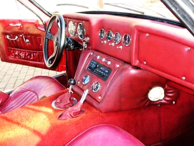 Early TVR Pictures - Page 28 - Classics - PistonHeads - The image features an interior shot of an old-fashioned car with a luxurious touch. The car's dashboard and steering wheel are red, giving it a vintage appeal. The steering wheel has a logo at the center, indicating the brand of the car. The interior also boasts a unique feature: a red handbag is resting on the driver's side, adding a surprising element to the composition. The car seems well-maintained, indicative of the owner's pride in their vintage vehicle.