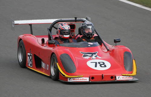 Look What I Just Came Across - Page 1 - Radical - PistonHeads - The image showcases a vibrant red race car speeding along a racing track. The car stands out with a black hood and a distinctive number "78" prominently displayed. Inside the cockpit, two drivers can be seen. Both drivers are wearing race suits and helmets with visors pulled up, indicating they are fully equipped for the high-speed race. The tension of the moment is palpable as the car and its drivers are captured in the midst of a swift maneuver on the track.