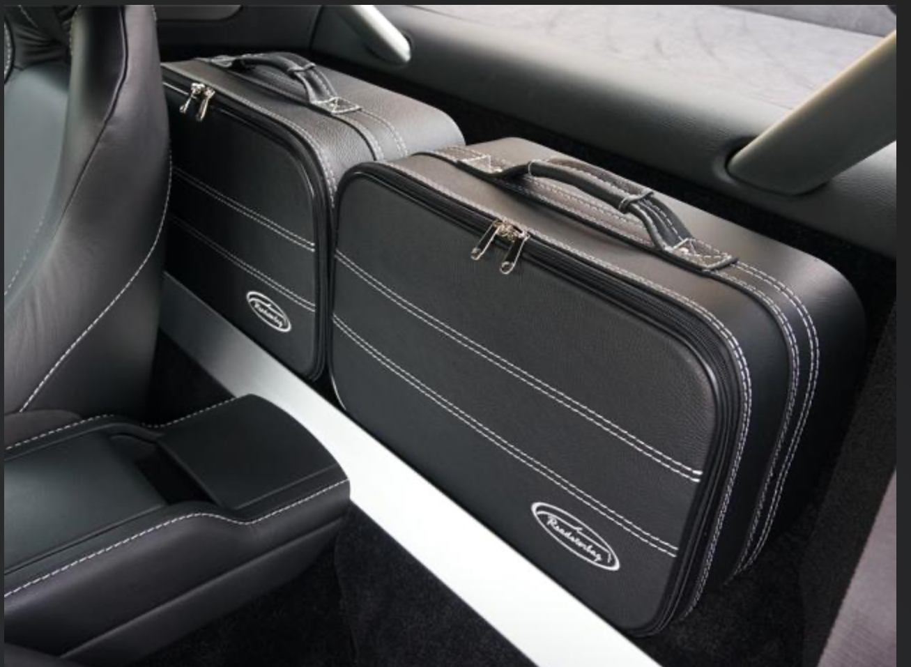 Pistonheads - The image shows a black briefcase sitting in the back of an SUV. There are two cases, one larger and one smaller, both with white piping on them. The interior of the car has a clean look with a black center console and leather seats. On the right side of the photo, there is a luggage rack mounted to the vehicle's roof. The image has a watermark with what appears to be an address or website URL.