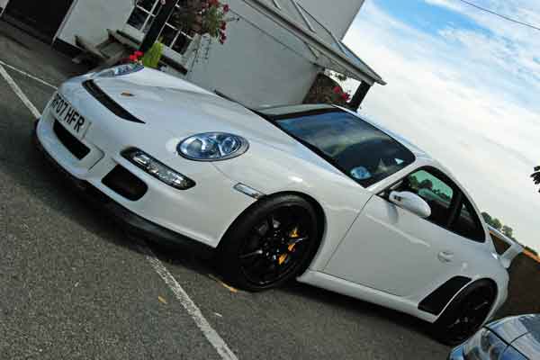 A car parked next to a parking meter - Pistonheads - The image presents a very sleek white sports car parked at a house or a motel. The car has a streamlined shape with aerodynamic lines, indicative of a modern design. The headlights are prominent, hinting at the vehicle's racing or high-performance capabilities. Its wheels are alloy, painted in a color that contrasts with the white of the bodywork. A small flower plant can be seen in the foreground, adding a touch of life to the scene.