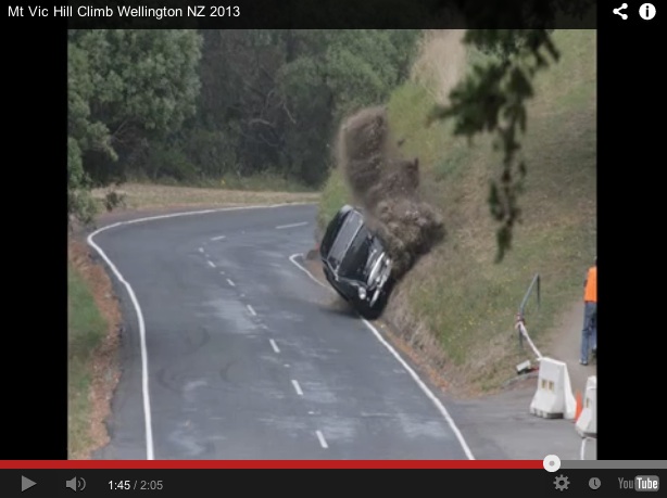 Healey bent on Hill Climb - Page 1 - New Zealand - PistonHeads - The image appears to be a still from a video, specifically a dashcam video, as indicated by the YouTube logo in the lower right corner and the anticipated duration at the bottom. It shows a vehicle, which seems to be a car, in motion driving down a road. The road is arched gracefully and has a white center stripe. There is dense vegetation on either side. The camera angle suggests that the dashcam is mounted on the windshield of the vehicle, capturing the vehicle's path down the road. The vehicle's position is tilted sideways, indicating that it is either in the process of a turn or has lost control, suggesting a potentially hazardous situation.