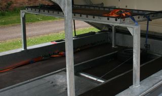 Sort Trailer Pistonheads - The image captures a neat and organized storage area. This area features two metal shelves supported by sturdy metal poles. A dark tarp covers the floor, contributing to the clean and utilitarian aesthetic of the space. Tucked safely underneath these shelves rests a bicycle, its vibrant orange color contrasting with the otherwise muted tones of the storage area.