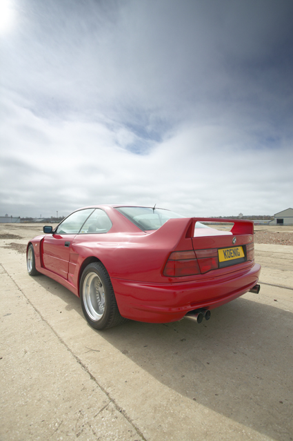 Show Pistonheads Bmw - The image depicts a close-up of a red sports car parked on a concrete surface under a partly cloudy sky. The car is adorned with a spoiler and a high-downforce exhaust, indicative of its racing capabilities. The vehicle's sleek design and vibrant red color make it the focal point of the image. In the background, soft-focus clouds add depth to the scene, and a skyline can be faintly seen in the distance.