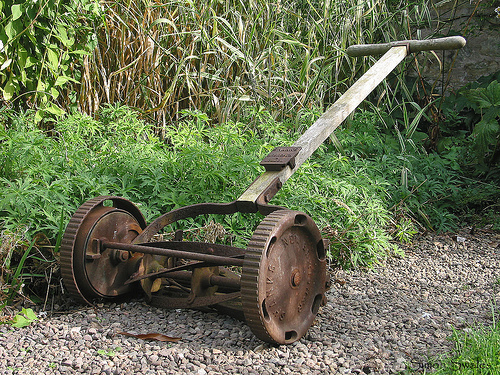 Paddleshift thoughts - Page 1 - Radical - PistonHeads - The image depicts a large, rusted metal plow leaning against a rocky area with plants and shrubbery. It features two large wheels with iron treads, a straight and narrow wooden handle, and metal pieces that connect the wheels to the handle. The plow is positioned to one side, indicating that it may have been discarded or is currently out of use. The surrounding environment suggests a natural, outdoor setting.