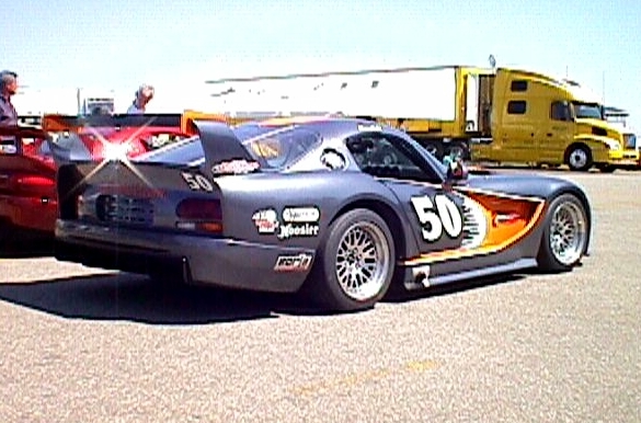 A truck is parked on the side of the road - Pistonheads - The image portrays a dynamic scene at a car show. At the center, a striking black racing car with "50" emblazoned in orange and white on its sideplane raises attention. Adjacent to it, a classic red convertible sports car adds a splash of color to the surroundings. Both cars are parked side by side, giving a sense of a comparative display. In the background, a large semi trailer hints at the diversity of vehicles present at the event. The ground appears to be a gravel lot, typical of outdoor car displays, enhancing the authenticity feel of the show.