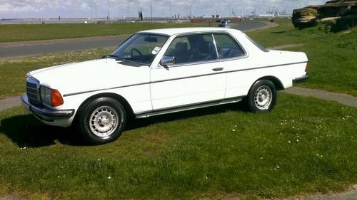 Classic (old, retro) cars for sale £0-5k - Page 218 - General Gassing - PistonHeads - This is a color photograph of a white Mercedes-Benz 280 sports car parked on a grassy area surrounded by a concrete pathway. The car is positioned at an angle, with its front driver's side facing the camera. It has prominent rear fenders, dual circular tail lights, and a distinctive indent in the center of the hood. Black rubber tires with five-spoke alloy wheels are mounted on the car. Its metallic exterior gleams under the sunlight, and the vehicle appears to be in good condition with no visible damage or scratches. There is a clear sky in the background indicating fair weather, and the scene suggests the vehicle is parked during the daytime.