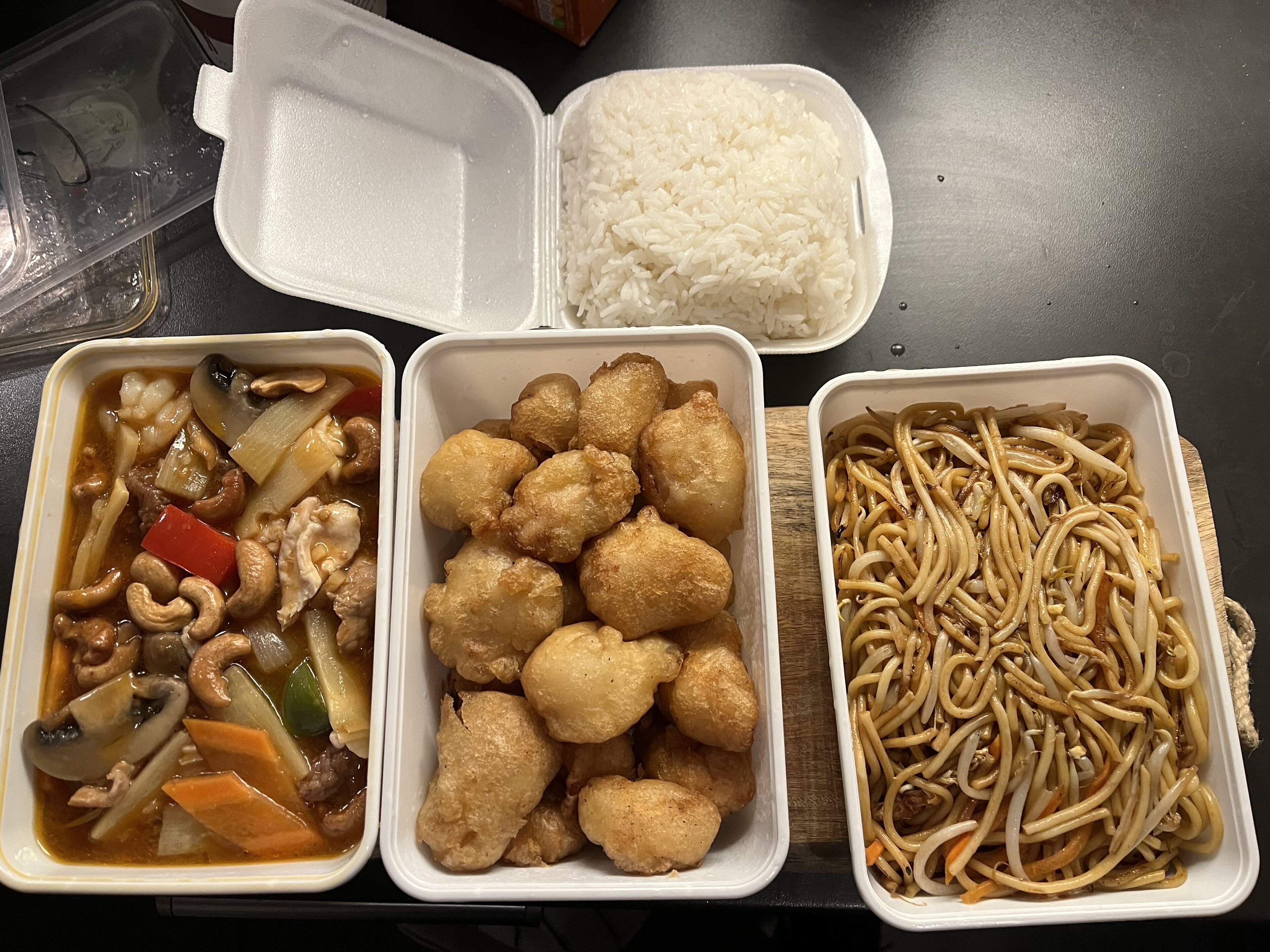 Dirty Takeaway Pictures (Vol. 4) - Page 378 - Food, Drink & Restaurants - PistonHeads UK - The image captures a delightful assortment of Chinese takeout food items, neatly arranged in disposable trays. On the left side, there's a tray filled with fluffy white rice, accompanied by a serving of chicken and mushrooms in another container. 

Moving towards the center, we find two trays laden with Chinese dumplings, their soft, rounded edges contrasting with the crisp packaging they come in. Further to the right, there are more trays showcasing other mouth-watering dishes. One tray features a vibrant stir-fry dish, while another contains what appears to be fried noodles with vegetables and meat. 

The food items are presented on a table, suggesting they are ready to be enjoyed. The variety of colors and textures suggests a balanced meal, full of different flavors and ingredients.