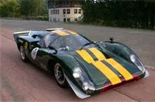 A blue car parked in a parking lot - Pistonheads - This is a photograph of a vintage racing car captured in daylight on a concrete road. The car is predominantly black with a bold yellow stripe across its center, perhaps indicating a racing number or team color. Its design suggests it is a sports car, likely based on a specific era of motor racing. The vehicle's shape is aerodynamic, with a nose that is pointed and angled for enhanced airflow. The car appears to be in motion, based on the slight blur on the edges, creating a dynamic sense of speed.