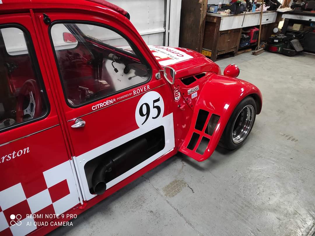 Pistonheads - The image shows a vibrant red race car parked indoors. The car is adorned with various stickers and sponsor logos, indicating it's ready for competition. It features a prominent number "95" on the side, which could represent its racing class or identification within the team. The setting appears to be a workshop or garage, given the presence of workbenches in the background. A few tools and equipment are visible, suggesting this is a space where maintenance and preparation for races take place. There's also a person present in the background, possibly a mechanic or crew member associated with the car.