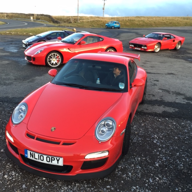 Great drive out today to Hartside Cafe - IN NOVEMBER !!! - Page 1 - Supercar General - PistonHeads - The image captures a dynamic scene on a tarmaced runway, where three cars have gathered. The focal point is a vibrant red Porsche sports car, which is turned towards the left, giving angular depth to the composition. It proudly displays a NLIO OPY license plate, suggesting it's either on duty or part of an association of similar vehicles.

In the background, parked side by side, are two more sports cars. One is a sleek black vehicle, and the other sports a striking yellow reflecting in its polished surface. Their positions, parked parallel and slightly further away, add a sense of scale to the scene. Despite the image's energy, there's no clear sign of movement or activity, suggesting a moment of anticipation before the cars' engines roar to life and they speed away into the distance.