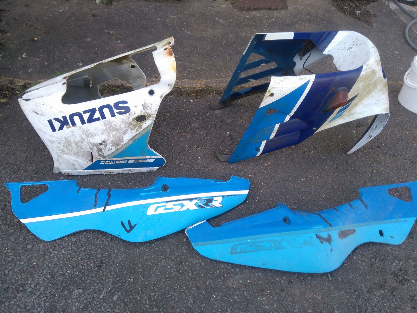 First Love Revisited - Page 1 - Biker Banter - PistonHeads - The image shows a trio of motorcycle fairings lying on a paved ground, indicating they have been removed from their respective motorcycles. The fairings display signs of use and wear, which could suggest they are second-hand or replacement parts. The colors are predominantly white and blue, with varying degrees of dirt or paint flaking. Some parts of the fairings have scratch marks, suggesting they have seen some rough handling or impacts. The presence of numerical characters indicating branding or identification numbers are visible on one of the fairings.