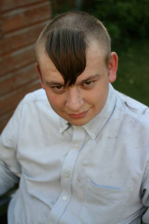 A young boy wearing a tie and a shirt - Pistonheads - The image captures a young man who sports a unique hairstyle. His haircut is of a bowl shape, with one long, wispy, and noticeable side hair that creates an interesting contrast with his otherwise shaved head. He is dressed in a white shirt with a blue pocket, which adds a touch of color to his outfit. The man is casually posing, looking directly into the camera with an relaxed expression. In the background, there's a blurred building, suggesting that the photo might have been taken in an urban setting.