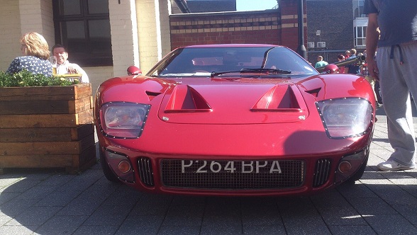 Camberley Town Centre car show - Page 1 - Thames Valley & Surrey - PistonHeads - The image features an open-top red sports car parked on a sidewalk. The car, which appears to be a sports car, is vibrant red with a sleek design. The license plate of the car, P204 BPI, can be seen prominently. Being a sunny day, there's some strong sunlight casting shadows. The setting is urban, with a few pedestrians and plants visible in the background.