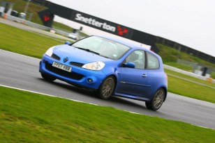 Local photo locations - Page 1 - East Anglia - PistonHeads - The image features a blue Renault Clio car on a racing track. The car is captured in motion, likely during a lap. It's positioned slightly off center, with the left front tire more prominently featured than the others. The background of the image showcases a partially visible race track sign advertising Snetterton, suggesting the location of the event. The car's speed and trajectory hint at a dynamic and exciting scene of motorsport competition.