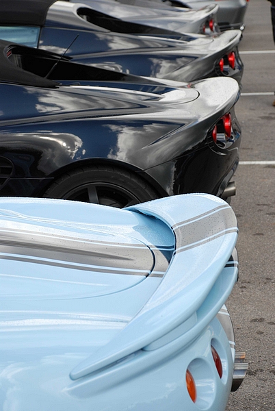 Goodwood Breakfast Club, Pre 1966 classic sunday - Page 1 - Goodwood Events - PistonHeads - The image shows a group of luxury sports cars. The cars are parked parallel to each other in what appears to be a parking lot. The cars are colored in shades of black and blue. The vehicle in the foreground appears to be a convertible with the top up, reflecting the light around it. The reflection of a cloudy sky is visible on the polished surfaces of the cars.