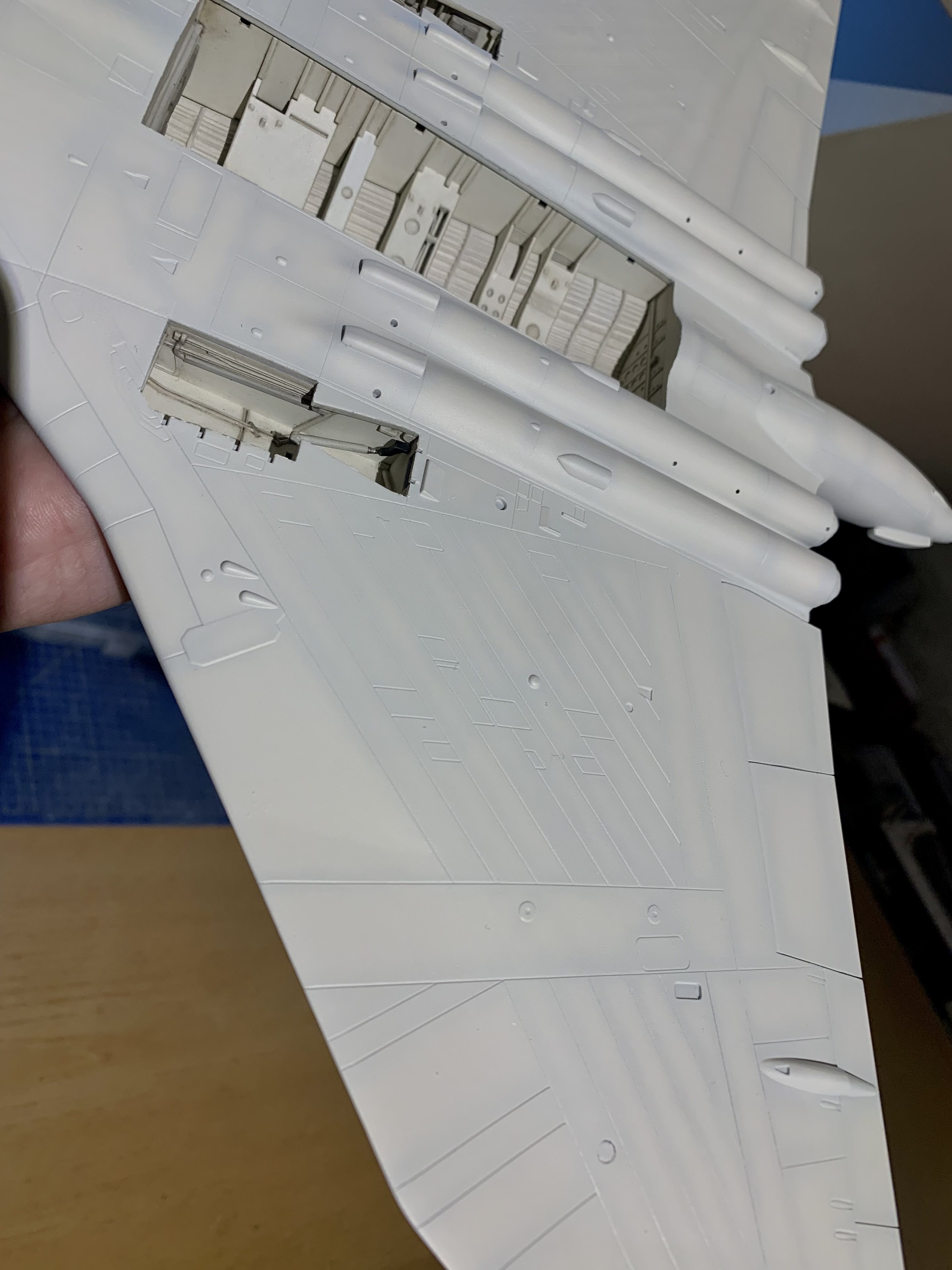 Airfix 1:72 Vulcan B.2 - Page 16 - Scale Models - PistonHeads UK - The image shows a model airplane that is in the process of being assembled. It appears to be an F-16 fighter jet, given its design and layout. The model is predominantly white and is laid out on a flat surface, possibly a table. There are visible details such as weapons bay doors and cockpit windows. To the right of the model, there's a hand holding up a small part that seems to be related to the model airplane, possibly a control yaw or some other component. The background is not very detailed but appears to be an interior space with a blue wall.