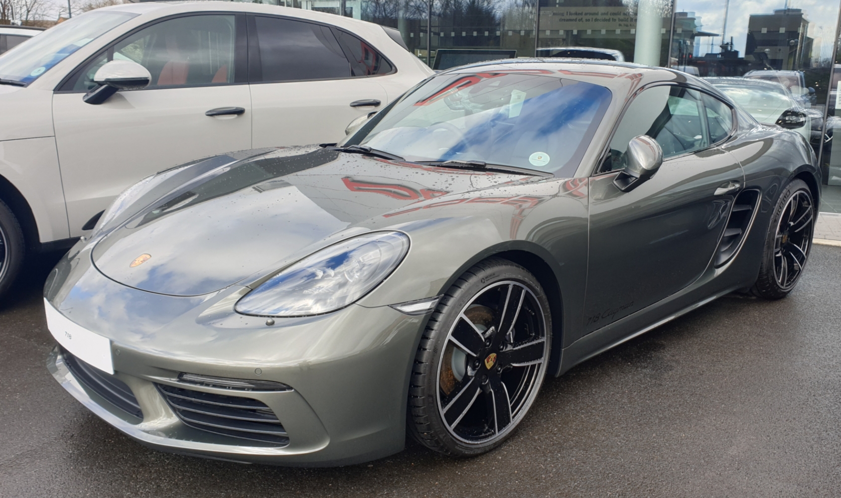 718 GTS 4.0…  - Page 52 - Boxster/Cayman - PistonHeads - The image shows a luxurious, silver-gray Porsche Cayman S sports car parked in a covered lot. The vehicle is sleek with a low center of gravity and features distinctive design elements such as the sloping rear roofline, side air vents, and multi-spoke alloy wheels. A prominent grille and badges on the hood indicate the model and possibly its engine specifications. The car's exterior is well-maintained with a shiny finish. In the background, there are two other vehicles, but they are not the focus of the image.