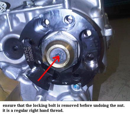 Help! - Page 1 - Radical - PistonHeads - The image shows the close-up of an automotive engine block with a focus on a mechanical component. There's a red arrow pointing towards a specific area, possibly indicating a point of interest or warning. Text present in the image reads, "ensure that the locking bolt is removed before undoing the nut. it is a regular right hand thread." The image provides guidance on a standard practice in engine maintenance.