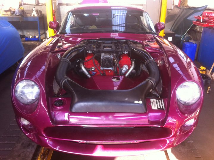 A red and black motorcycle parked in a parking lot - Pistonheads - This is a close-up real-life photograph of a vibrant pink sports car with the hood open, showcasing a mechanical interior that connects the engine to the drive wheels. The car appears to be in a workshop or garage, indicated by the presence of other equipment and tools in the background. The sunlight is filtering in, contributing to a glossy reflection on the car's bodywork. The car has distinctive design features typical of sports cars, including painted side mirrors and a headlight with a clear design.