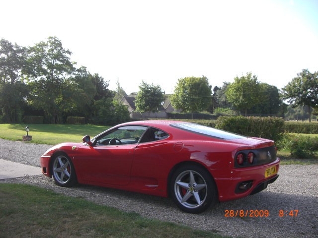 100,000 miles in my 360 - Page 1 - Supercar General - PistonHeads - The image captures a scene featuring a sleek red sports car parked on a pebbled driveway. The car is positioned at an angle, with its side profile visible. It has a black convertible roof, and a set of elegant rims adorn its wheels. The grassy area behind the car is lush and green, complete with trees that contribute to a serene, natural setting. The timestamp on the image indicates it was taken on August 28, 2009, at 8:47.