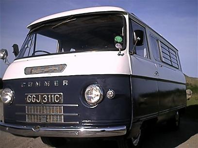 British Leyland -They were crap and they knew they were. - Page 32 - General Gassing - PistonHeads - The image shows a vintage Volkswagen bus with a flat front, parked against a clear blue sky. The automobile has a distinctive white and blue striped pattern across its lower half. The license plate reads "GJ31C," and there's a sticker on the windshield. The vehicle's side panel has a functioning window, and the overall body of the car appears to be in good condition. The vw bus is commonly associated with a nostalgic and retro style.