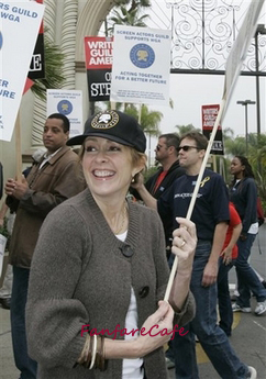 120682 - The image shows a woman standing in a crowd of people who appear to be participating in a city dweller's rally. She is smiling and holding a placard over her head. On the placard, there is text that reads "Defend Oprah's Vow." Around her neck, she is wearing a necklace. There are other individuals in the image, suggesting a public demonstration or event. The location seems to be an urban environment, possibly on a street, given the presence of buildings and a wrought iron gate in the background.