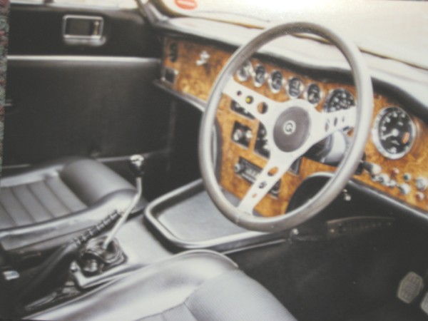 Invader Estates Pistonheads - This image captures the interior of a classic, possibly vintage automobile. The car's interior is dominated by wood panels on the dashboard and the console, giving it an antique feel. The steering wheel, detailed with various buttons and dials, is situated in the center of the photo and appears to be made of metal. There's also a gear stick visible in the lower left corner of the photo, adding to the car's old-time charm.