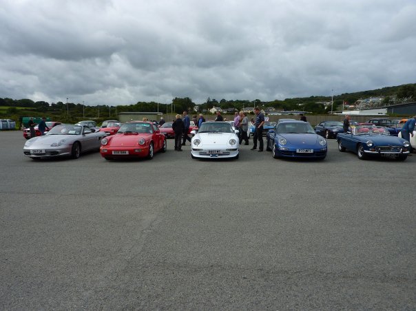 September Pistonheads Pembrokeshire County - The image captures a lively scene at a parking lot where a group of people, approximately six in total, are interacting with various cars on display. These cars range from classic to sports and luxury models, including iconic brands like Porsche and Ferrari. The people appear to be examining, admiring, and possibly discussing the cars, suggesting this could be an auto show or a public gathering. Despite the multitude of vehicles and attendees, the atmosphere seems relaxed and engaging. Little noticeable detail about the location itself.