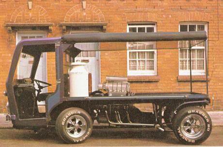 An old truck is parked in a parking lot - Pistonheads - This image features a vintage military transport jeep, painted in a dark color. The vehicle is parked beside a stone building with arched windows. A prominent feature of the jeep is a large black awning attached to the roof, providing shade for the interior. Inside the jeep, a bench seat and possibly other seating can be seen. The image captures a scene from a past era, as suggested by the style of the jeep and the architecture of the building.