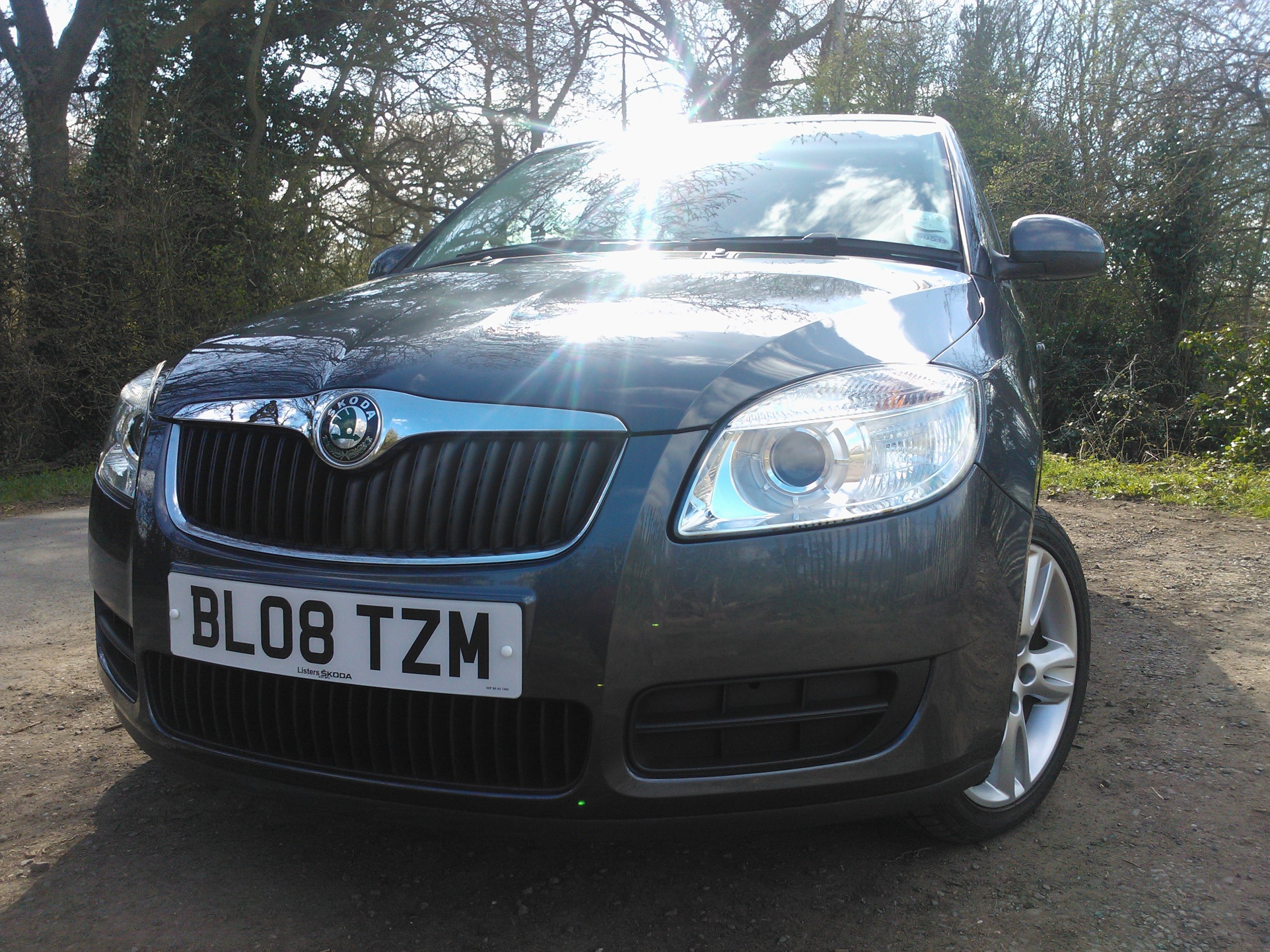 Skoda Fabia SE - Page 3 - Readers' Cars - PistonHeads - The image shows a dark-colored Volkswagen hatchback car parked on a gravel surface. The vehicle has a shiny finish, reflecting the sunlight. It features a round badge on the front grille, consistent with the Volkswagen logo, and a standard number plate indicating the registration is from Tameside. The car has standard alloy wheels and a sleek design, typical of modern German cars. In the background, there are trees and shrubs, suggesting that the car is parked in an outdoor or rural area during daylight.